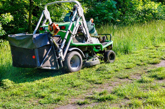专业拖拉机草坪上割草机割高草沿着公园格罗夫攀爬的坡和管理实用程序工人复制空间专业拖拉机割草机驱动公共实用程序工人爬的坡和割高草