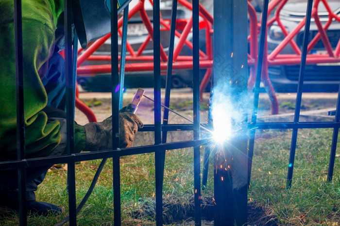 明亮的火花从电焊接散射不同的方向对的背景工作焊机和金属栅栏模糊明亮的闪光金属焊接的背景金属栅栏