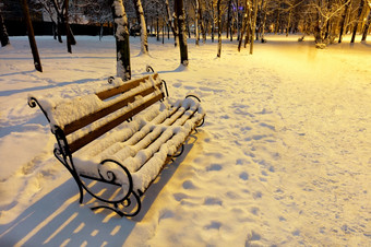 空棕色（的）<strong>木板</strong>凳上与金属装饰栏杆的雪下的温暖的光街灯冬天晚上城市公园<strong>木板</strong>凳上冬天城市晚上公园覆盖与雪和照亮的温暖的光街灯