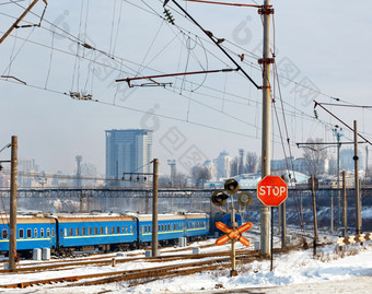 红色的停止标志铁路穿越对的背景铁路跟踪蓝色的火车车厢和城市景观的入口冬天城市红色的停止标志的铁路穿越对的背景的铁路站和建筑的冬天城市