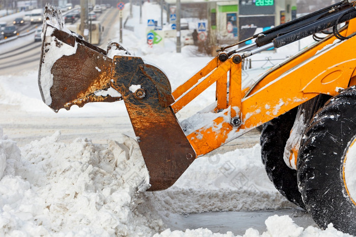 大桶黄色的拖拉机铲子雪从城市路对的背景城市街和通过汽车的拖拉机与的帮助大金属桶清洗的车道城市街从丰富雪