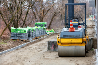 紧凑的路辊站建设网站与夷为平地沙子基地为的后续铺设铺平道路板对的背景栈灰色的铺平道路板和的春天灌木丛城市公园模糊路辊坚固建筑网站与人行道上下建设的背景和栈灰色的铺平道路板模糊