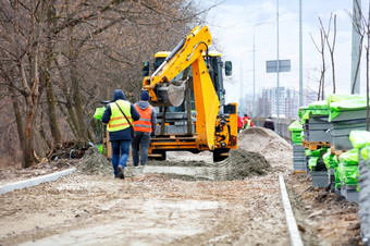 橙色路挖掘机和集团工人准备桑迪基地为铺平<strong>道路</strong>板走路径沿着城市街春天下午工作团队使用路挖掘机卸载栈铺平<strong>道路</strong>板的一边的路为后续铺平<strong>道路</strong>