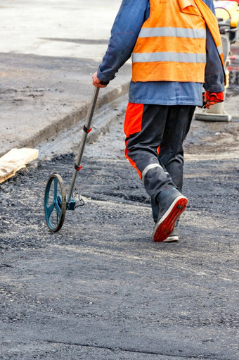 路服务工人谁措施路距离与测量轮决定了的要求量沥青为铺平道路垂直图像复制空间路服务工人措施的<strong>工地现场</strong>与电子测量轮