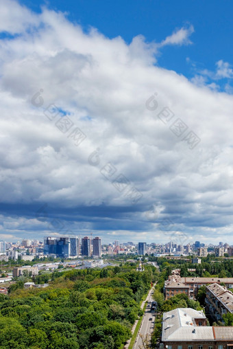 视图从高度的城市基辅的夏天中午绿色公园的前景老住宅区域和新建筑的地平线对蓝色的天空与突出白色和灰色的云垂直图像复制空间大白色和灰色的云隐约可见在绿色公园的老住宅区域的城市和新建筑的地平线对的背景明亮的