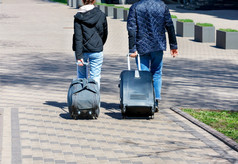 年轻的夫妇男人。和女人走沿着的鹅卵石人行道上旅行阳光明媚的一天携带旅行袋和手提箱轮子复制空间年轻的夫妇旅行者走沿着的鹅卵石人行道上携带旅行袋和手提箱轮子