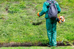 工人绿色工作服和背包他的回来割的草与工业汽油微调城市公园复制空间工人割绿色草与汽油微调