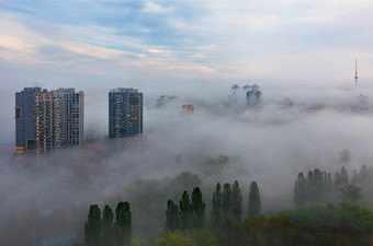 多雾的早....包膜的睡觉城市基辅住宅高层建筑和绿色公园与一瞥的蓝色的天空厚雾的后代的早期早....的睡觉城市和延伸之间的住宅高层建筑和在的绿色公园