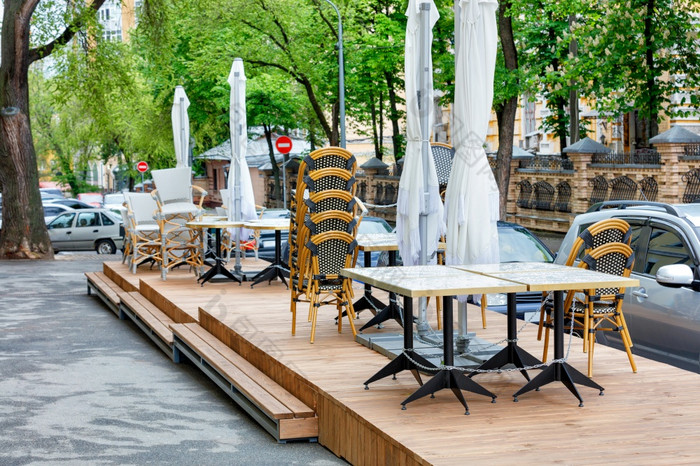 的木平台的关闭夏天咖啡馆在那里花园家具表椅子和雨伞是链接对的背景的城市街和通过汽车的户外咖啡馆户外区域关闭户外家具表椅子和雨伞是链接在一起
