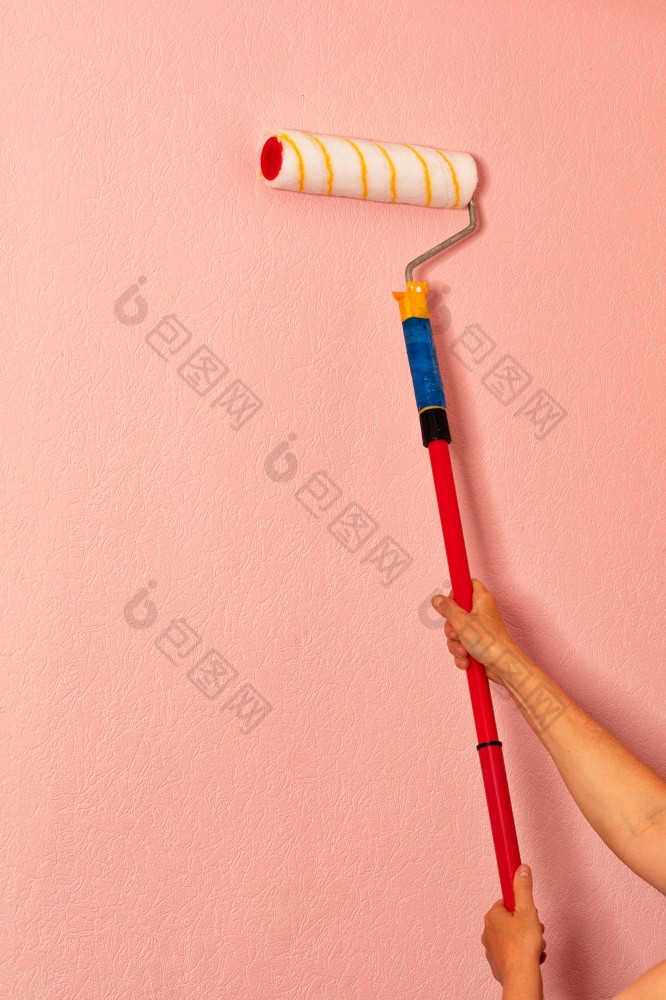 女手的画家持有油漆辊长伸缩杆对的背景粉红色的墙垂直图像复制空间羊毛油漆辊的女手画家对的背景粉红色的墙