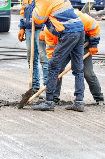 路工人橙色工作服使用铲子删除碎片从的老路表面路工人使用铲子清洁的老路表面的巷道