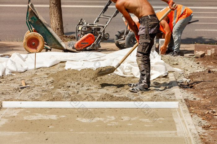 工人水平的基金会与沙子和铲下木水平为铺设铺平道路板对的背景的工作场所夏天一天复制空间实用程序工人准备网站为铺设铺平道路板夏天一天