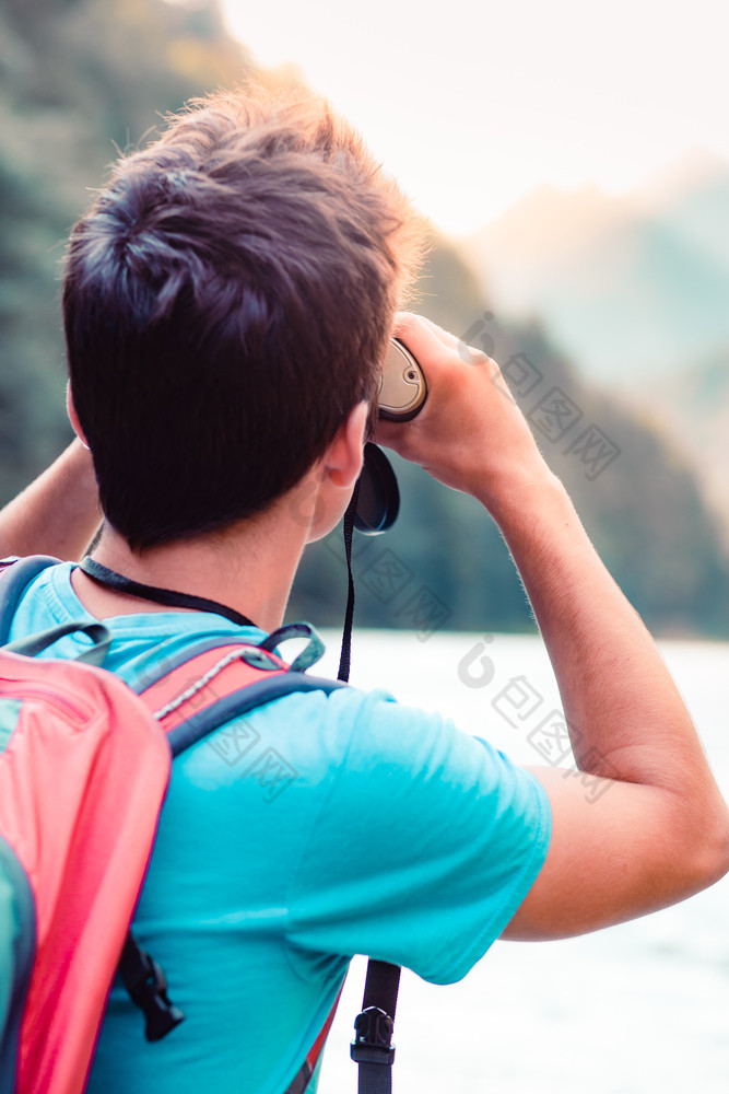 年轻的旅游与背包看起来通过双筒望远镜山山峰站岩石在河男孩花假期山流浪的与背包穿体育夏天衣服