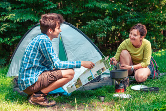 支出假期野营女人准备餐户外男人。持有地图规划下一个旅行
