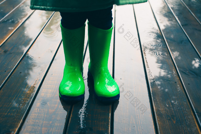 特写镜头腿孩子站玄关穿绿色长筒靴和雨衣雨靴子明亮的绿色颜色