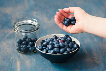女人把新鲜聚集蓝莓从Jar成小碗表格画蓝色的的背景