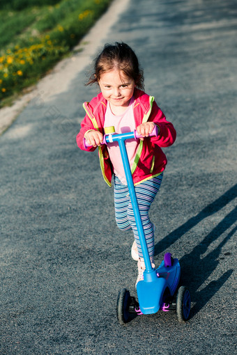 小可爱的女孩有有趣的骑踏板车玩在户外