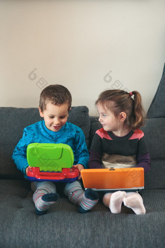 两个孩子们玩与笔记本电脑学习基本数字字符听起来和图片小女孩和男孩坐着沙发和玩在一起首页坦诚的人真正的时刻真实的的情况下