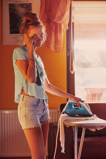 年轻的女人熨衣服她的衣服和会说话的<strong>智能</strong>手机同时站熨衣服董事会房间首页例程<strong>管家</strong>任务首页坦诚的人真正的时刻真实的的情况下