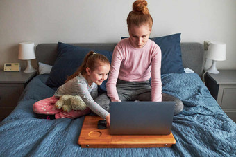 十几岁的女孩工作学校测试家庭作业远程她的移动PC从首页在新冠病毒检疫公司她的小妹妹女孩坐着床上前面电脑