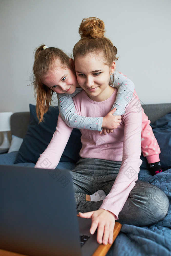 孙子十几岁的女孩和她的年轻的妹妹会说话的视频调用与granparents移动PC从首页在新冠病毒检疫女孩坐着床上前面电脑