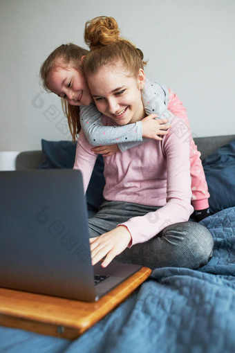 孙子十几岁的女孩和她的年轻的妹妹会说话的视频调用与granparents移动PC从首页在新冠病毒检疫女孩坐着床上前面电脑