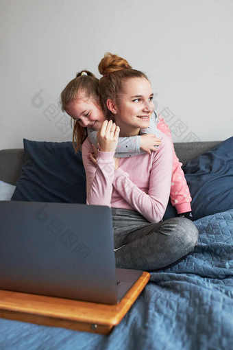 十几岁的女孩和她的年轻的妹妹玩学习移动<strong>PC</strong>支出时间在一起<strong>首页</strong>在<strong>新</strong>冠病毒检疫女孩坐着床上前面电脑