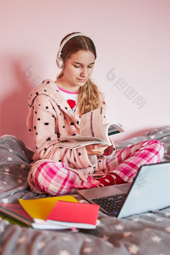 学生学习在线看教训远程听教授会说话的与同学们视频调用从首页在检疫年轻的女孩使用移动PC耳机书手册坐着床上