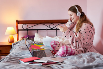 学生学习在线看教训远程听教授会说话的与同学们视频调用从首页在检疫年轻的女孩使用移动PC耳机书手册坐着床上