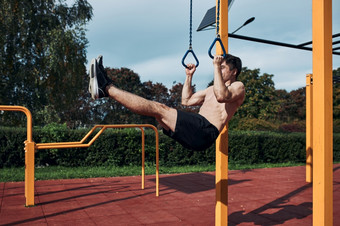 年轻的赤膊上阵男人。健美运动员做l-sit在他的锻炼现代健美操街锻炼公园