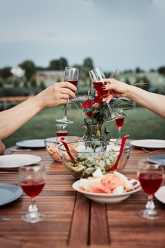 夫妇使烤面包在夏天户外晚餐首页花园手持有酒眼镜与红色的酒在表格与菜