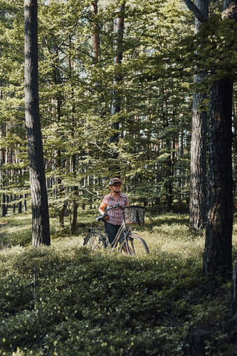 活跃的女人支出免费的夏天假期时间自行车旅行森林女人穿自行车头盔和手套持有自行车与篮子活跃的女人支出免费的夏天假期时间自行车旅行森林