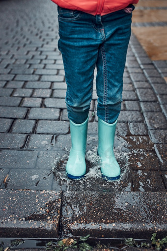 关闭腿小女孩跳水坑穿橡胶靴子走多雨的悲观的秋天一天孩子跳水坑穿橡胶靴子走多雨的悲观的秋天一天