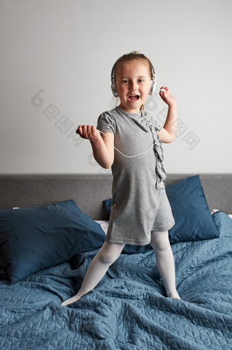 小女孩<strong>唱歌</strong>持有耳机绳模仿自己真正的歌手<strong>孩子</strong>有有趣的跳跳舞听音乐床上卧室首页