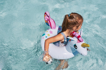 小女孩玩游泳池与充气橡胶环玩具的形状独角兽视图从以上孩子绿松石水游泳橡胶色彩斑斓的环小女孩玩游泳池与充气环玩具的形状独角兽