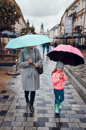 妈妈。和她的小女儿持有的粉红色的和蓝色的<strong>雨伞</strong>走市中心多雨的悲观的秋天一天女人和小女孩持有的<strong>雨伞</strong>走市中心多雨的悲观的秋天一天