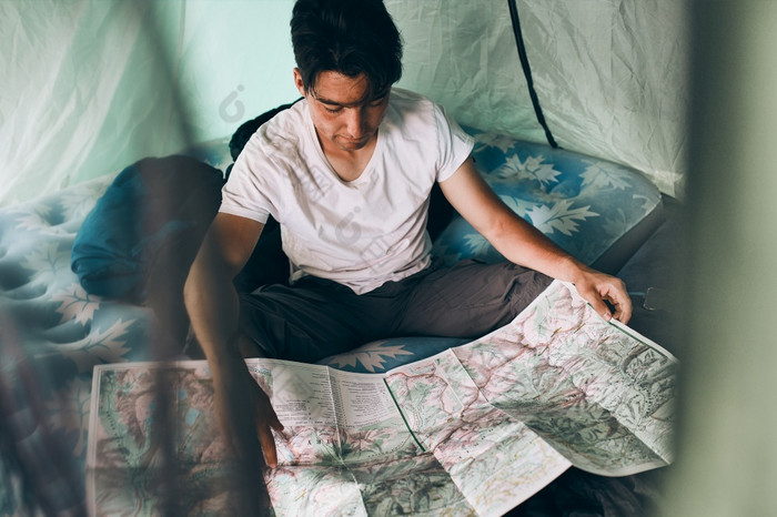 年轻的男人。看地图山小径规划下一个旅行夏天假期坐着帐篷野营概念营生活年轻的男人。看地图山小径规划下一个旅行夏天假期坐着帐篷野营