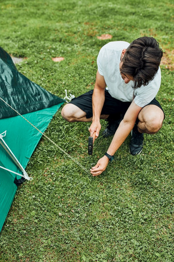 年轻的男人。把帐篷野营在夏天假期旅行少年把的股份成长满草的地面使用锤年轻的男人。把帐篷野营在夏天假期旅行