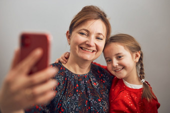 妈妈。与她的小女儿使视频调用使用移动电话保持距离女人和小女孩会说话的与亲戚快乐的家庭有有趣的采取自拍照片使用智能手机连接远程与家庭