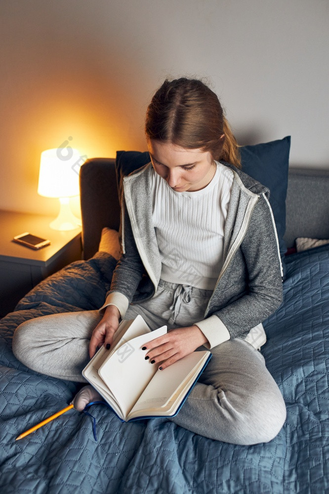学生学习首页年轻的女人使笔记阅读和学习从记事本坐着床上首页在检疫