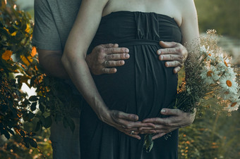 怀孕了女人和她的丈夫拥抱她的肚子站在户外包围自然怀孕期望母亲概念