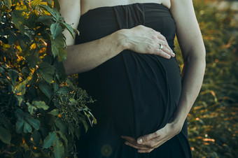 怀孕了女人拥抱她的肚子站在户外包围自然怀孕期望母亲概念