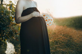 怀孕了女人拥抱她的肚子站在户外包围自然怀孕期望母亲概念
