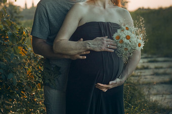 怀孕了女人和她的丈夫拥抱她的肚子站在户外包围自然怀孕期望母亲概念