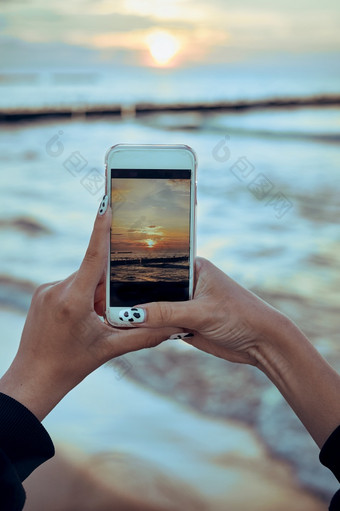 年轻的女人采取照片日落在海使用智能手机在夏天旅行后视图女孩持有智能手机和采取图片