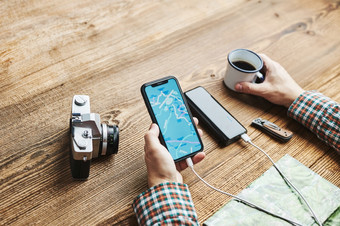 男人。规划下一个假期旅行而<strong>旅程</strong>搜索旅行目的地和路线使用导航地图移动电话充电智能手机与权力银行使用技术而旅行男人。坐着木表格与相机喝咖啡旅行计划概念男人。规划下一个假期旅行而<strong>旅程</strong>搜索旅行目的地和路线使用
