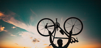 骑自行车的人轮廓与自行车提高了天空比赛和胜利概念