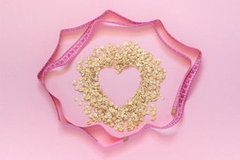 燕麦片形状心和转轮测量磁带粉红色的背景饮食概念前视图复制空间燕麦片形状心和转轮测量磁带粉红色的背景饮食概念