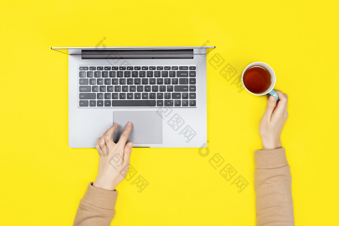 人工作打字移动PC电脑现代空间女手工作新移动PC明亮的黄色的背景与茶杯前视图平躺女手工作新移动PC明亮的黄色的背景与茶杯前视图平躺
