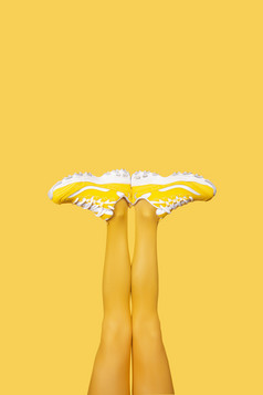 新黄色的女运动鞋长女人腿黄色的连裤袜孤立的黄色的背景单色流行艺术概念垂直横幅与复制空间新黄色的女运动鞋长女人腿黄色的背景垂直横幅与复制空间